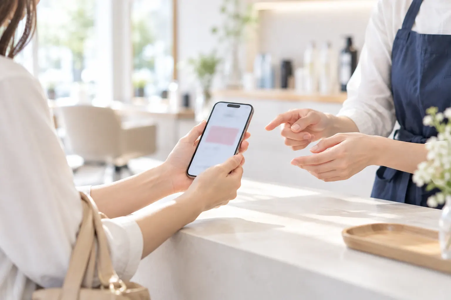 サロンの受付で、お客様がスマートフォンの画面をスタッフに見せている手元
